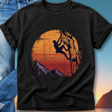 Silhouette of a climber on a mountain against a sunset, with purple mountains below.