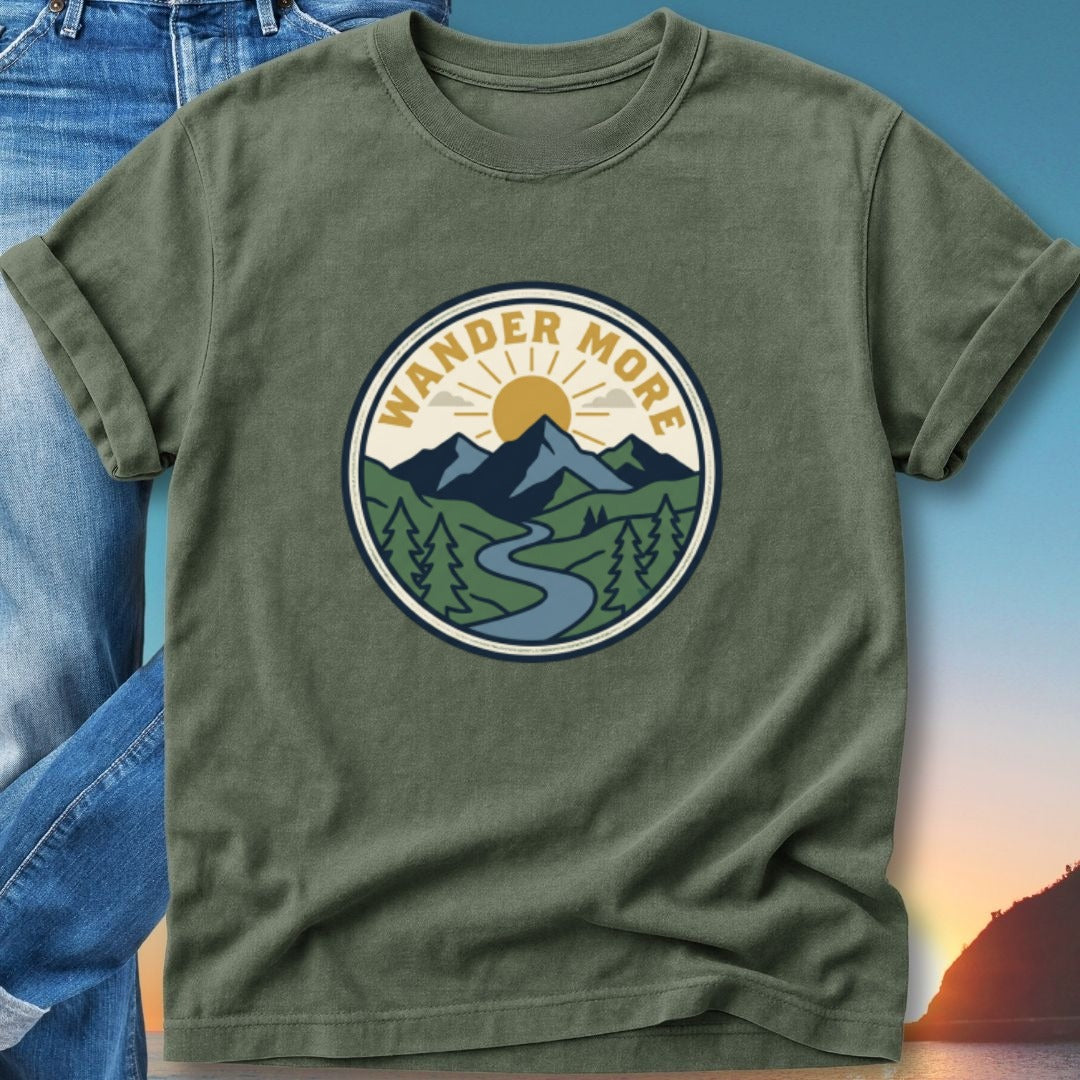 Olive green t-shirt with circular outdoor graphic: "WANDER MORE" text, mountains, sun, and river.