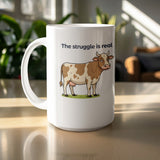 White mug with a cartoon cow and "The struggle is real" text.