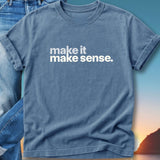 Blue t-shirt with "make it make sense." text, folded on jeans.
