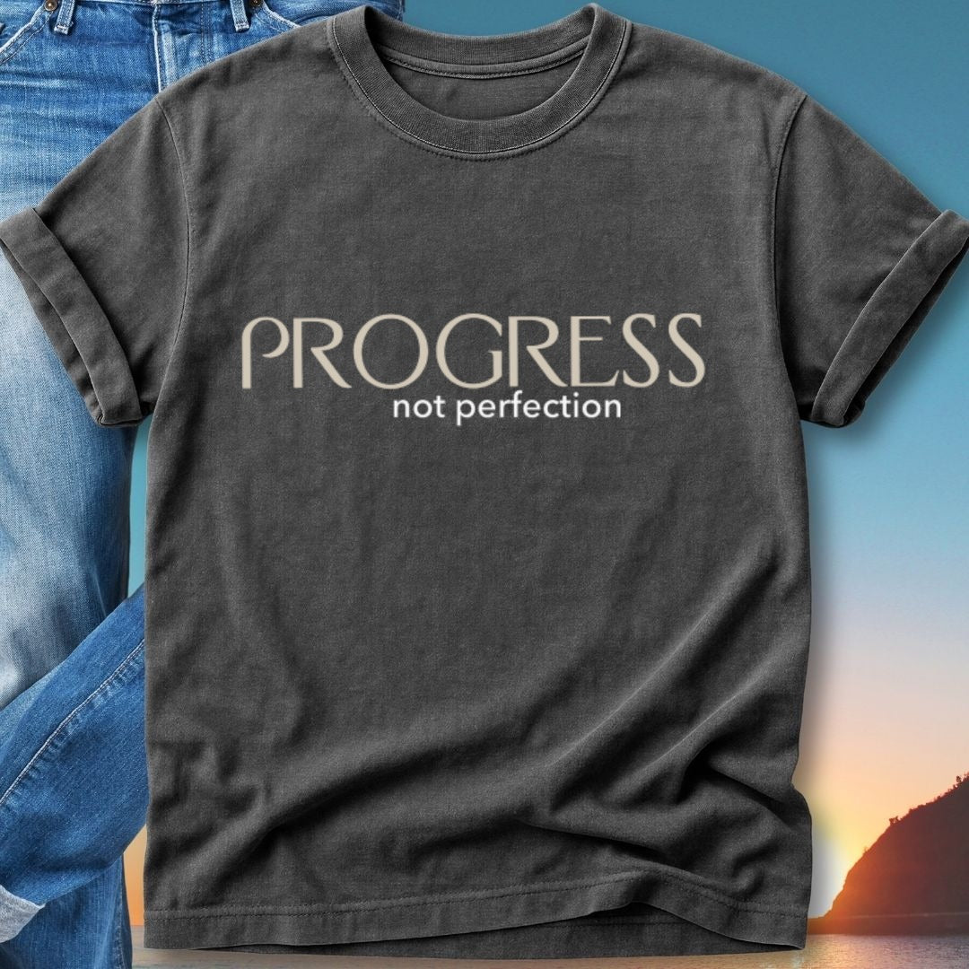 Charcoal t-shirt with "PROGRESS not perfection" text against a blurred sunset background.