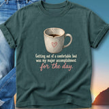 Dark teal t-shirt with a mug of coffee and text: Getting out of a comfortable bed was my major accomplishment for the day.