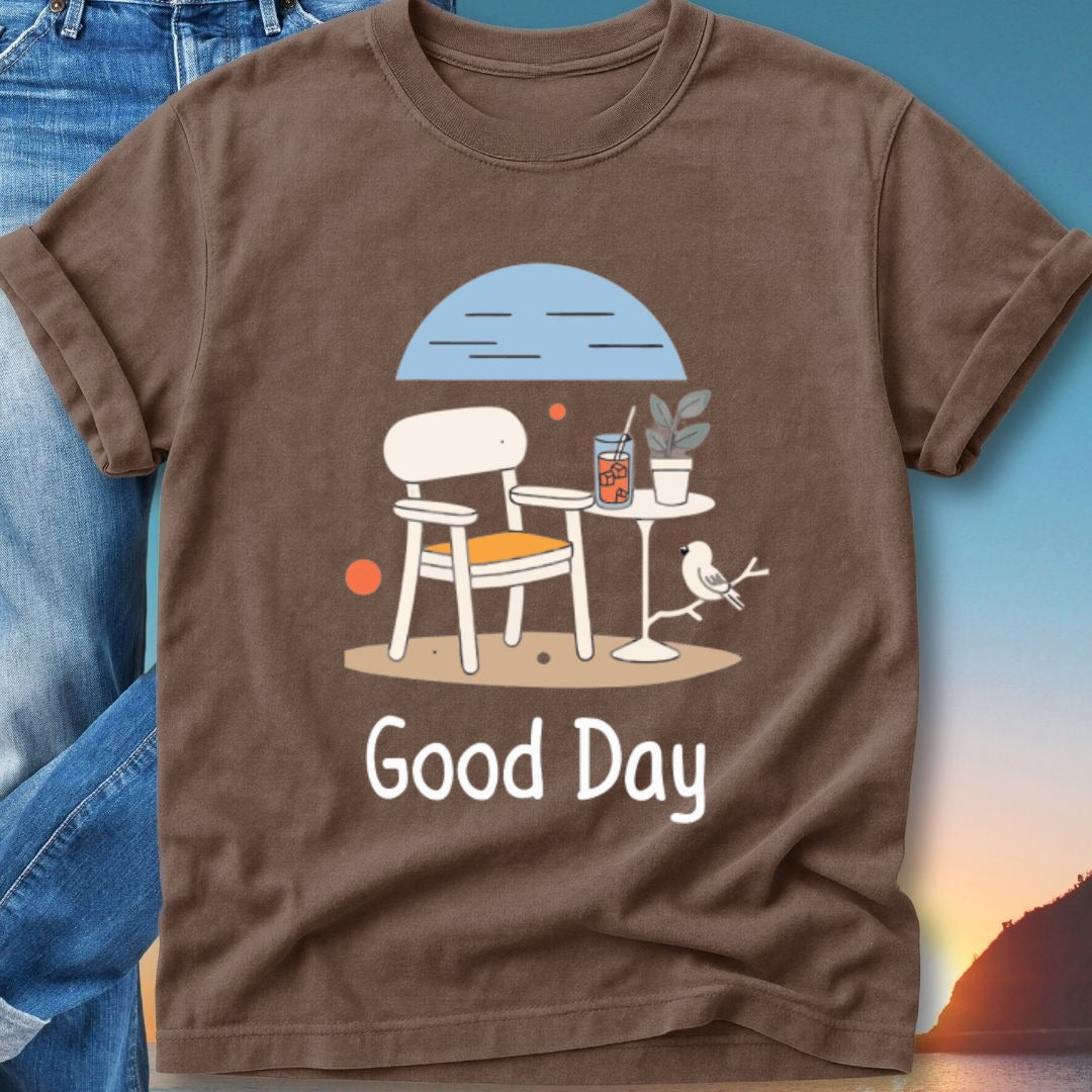 Brown t-shirt with a graphic of a chair, table, drink, and bird under a blue sky.
