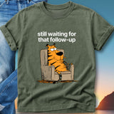 Olive green t-shirt with a cartoon tiger sitting in a chair, text reads "still waiting for that follow-up".