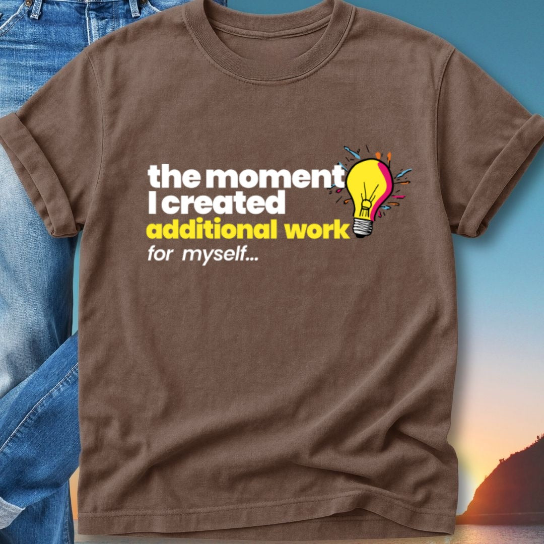 Brown t-shirt with text "the moment I created additional work for myself..." and a lightbulb icon.