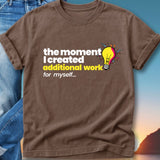 Brown t-shirt with text "the moment I created additional work for myself..." and a lightbulb icon.