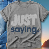 Grey t-shirt with "JUST saying" text, layered over jeans with sunset background.