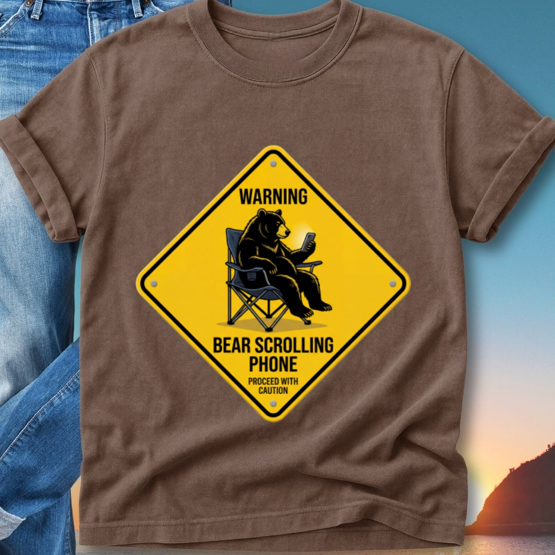 Brown t-shirt with yellow warning sign: Bear sitting in chair scrolling on phone.