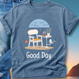 Blue t-shirt with a drawing of a chair, table, drink, and bird.