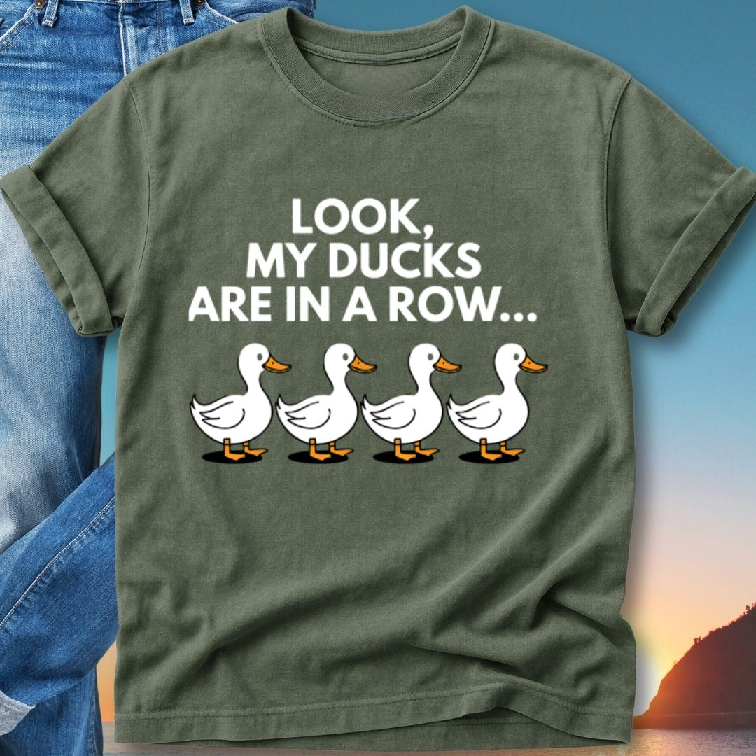 Green t-shirt with white cartoon ducks in a row and text that reads "LOOK, MY DUCKS ARE IN A ROW..."