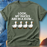 Green t-shirt with white cartoon ducks in a row and text that reads "LOOK, MY DUCKS ARE IN A ROW..."